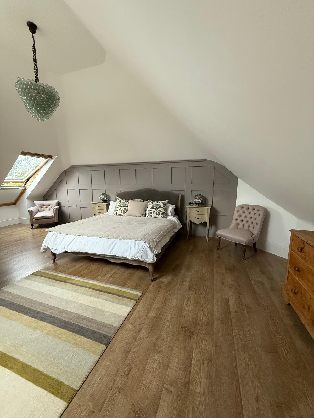 Loft bedroom with a panelled eaves wall, French-style bed, button-back chairs and a roof window