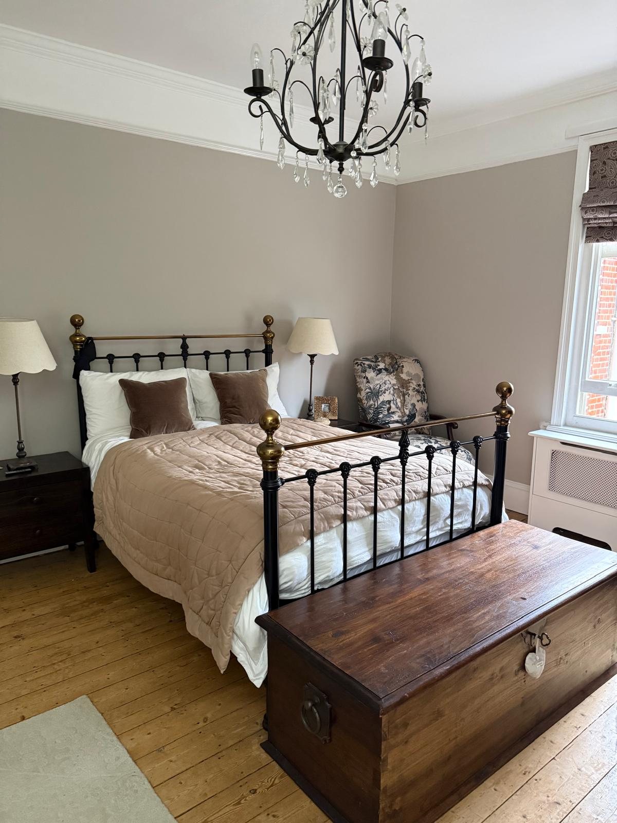 Bedroom with a black and brass bed, velvet cushions, crystal chandelier and antique chest
