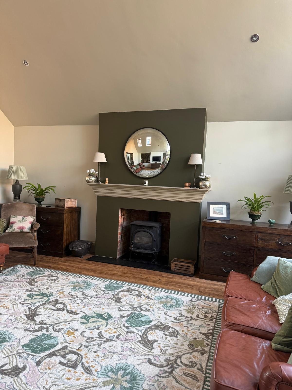 Drawing room with an olive chimney breast, convex mirror, wood burner and floral rug